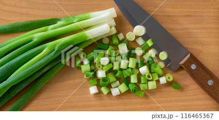 A top down view of chopped green onion on a wooden cutting board. Close up 116465367