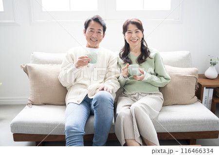 テレビや動画などを見るリビングでくつろぐ50代の夫婦の全身　話すカップルの正面の全身　カメラ目線 116466334
