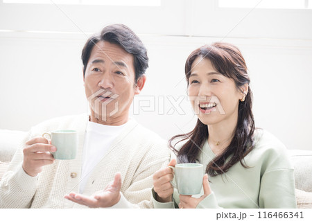 テレビや動画などを見るリビングでくつろぐ50代の夫婦の全身　話す会話するカップルの正面上半身 116466341
