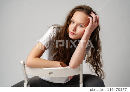 Curly girl model posing on a chair against gray background Curly girl model posing on a chair against gray background 116470377
