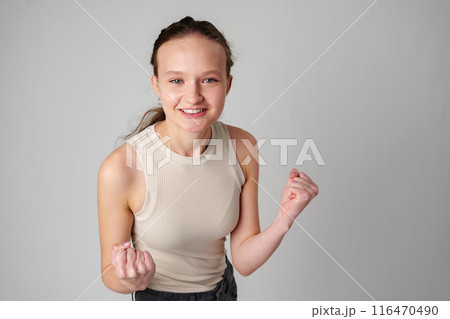 Young Woman in Casual Attire Smiling and Making a Fist Pump Gesture on a Plain Background Young Woman in Casual Attire Smiling and Making a Fist Pump Gesture on a Plain Background 116470490