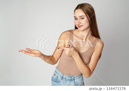 Young Woman in Tank Top Pointing at Something on gray background 116471576