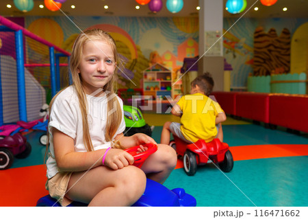 Young Girl Sitting on Toy Car in Play Room 116471662