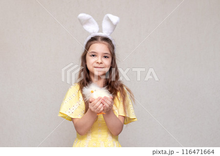 A girl with rabbit ears on her head with a basket of colored eggs and yellow flowers in her hands. Easter for a child. 116471664