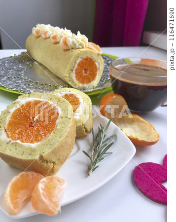 Cooking biscuit roll stuffed with ricotta and mandarin. Ready roll lies on a platter. Next on the saucer is a cut piece of roll. 116471690