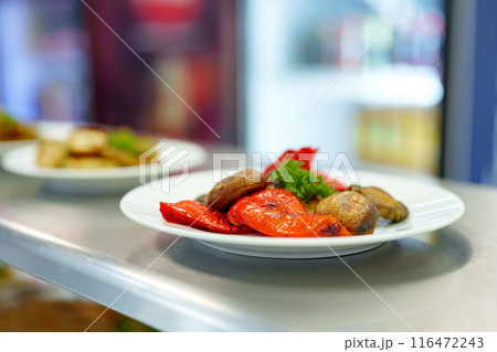 Vibrant Grilled Vegetables Served on a White Plate in a Busy Restaurant Kitchen Vibrant Grilled Vegetables Served on a White Plate in a Busy Restaurant Kitchen 116472243