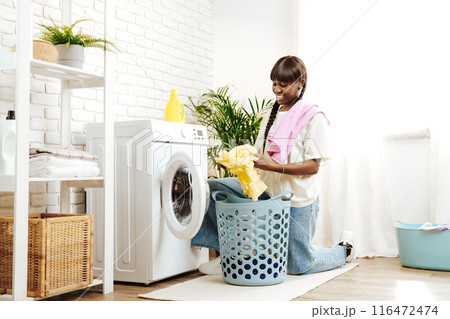 African Woman Folding Laundry After Washing Clothes in Modern Laundry Room 116472474