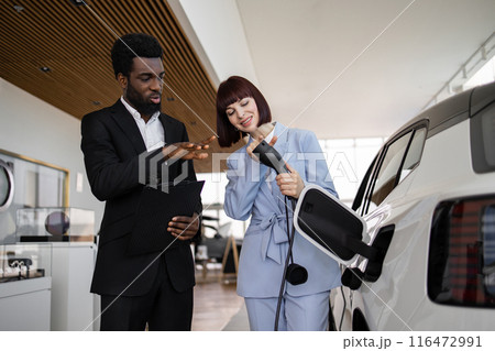 Dealer sells electric SUV to business woman at car dealership Dealer sells electric SUV to business woman at car dealership 116472991