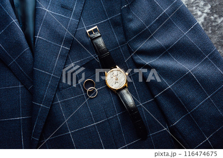 Groom's wedding details. Watch, rings and belt placed on a checkered jacket 116474675