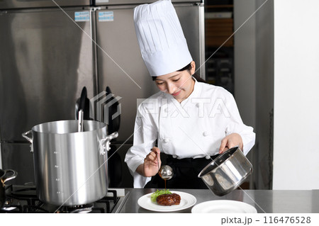 料理を皿に盛り付ける若いアジア人の女性調理師 116476528