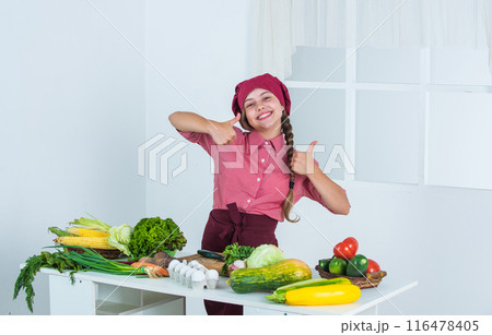 best day ever. full of vitamins. kid wear chef uniform and hat. teen girl preparing meal. fresh raw vegetables. time to eat. thumb up. happy child cooking in kitchen. healthy and organic food only 116478405