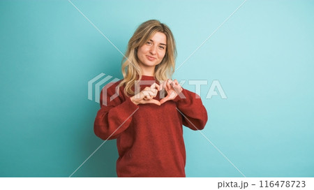 Happy woman blowing kiss and showing heart gesture in blue studio Happy woman blowing kiss and showing heart gesture in blue studio 116478723