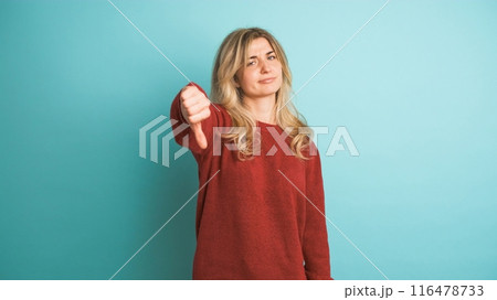 Sad young woman showing thumb down in blue studio Sad young woman showing thumb down in blue studio 116478733