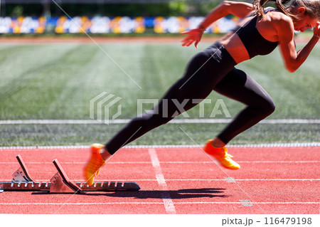Female sprinter launches from the starting blocks with explosive power Female sprinter launches from the starting blocks with explosive power 116479198