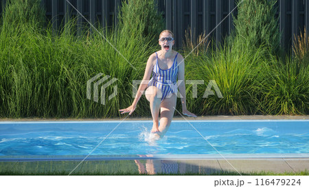 A teenage girl in a striped swimsuit jumping into a backyard pool, enjoying a sunny day. A teenage girl in a striped swimsuit jumping into a backyard pool, enjoying a sunny day. 116479224