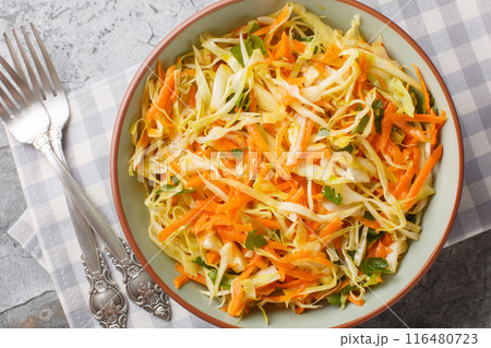 Cabbage salad with carrots dressed with vinegar and olive oil close-up in a bowl. Horizontal top view 116480723