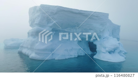 Towering melting iceberg drifting morning mist in Antarctica. Massive iceberg floating ocean in fog. Glacier melting, climate change impact on polar environment. Antarctic travel. Drone shot close up 116480827
