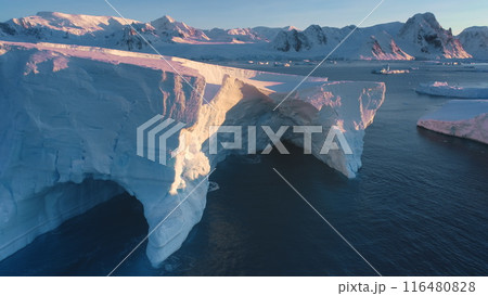 Large impressive iceberg cave in arctic sunset landscape. Huge high ice glacier at polar nature environment. Ecology, melting ice, climate change, global warming. Close up aerial drone shot 116480828