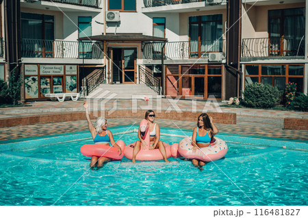 Three women are sitting on inflatable floats in a pool. Scene is lighthearted and fun. Three women are sitting on inflatable floats in a pool. Scene is lighthearted and fun. 116481827