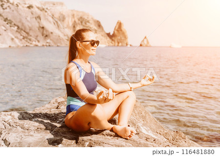 Yoga on the beach. A happy woman meditating in a yoga pose on the beach, surrounded by the ocean and rock mountains, promoting a healthy lifestyle outdoors in nature, and inspiring fitness concept. 116481880