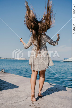 woman with long hair is standing on a dock by the water. She is wearing a dress and she is enjoying the view. woman with long hair is standing on a dock by the water. She is wearing a dress and she is enjoying the view. 116482373