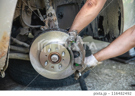 Mechanic man installing new brake disc and brake pads on car, car repair 116482492