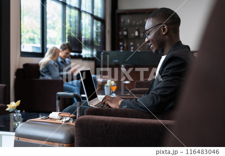 Man with suitcase sitting in airport waiting area. African businessman using laptop and waiting for his flight 116483046