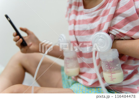 Mom pumping breastmilk to bottle and use cell phone to surf internet 116484478