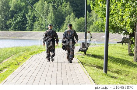 Two male police officers with black uniforms seen from behind walking in the city park Two male police officers with black uniforms seen from behind walking in the city park 116485870
