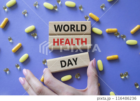 World Health Day symbol. Concept words World Health Day on wooden blocks. Beautiful purple background with pills. Doctor hand. Healthcare and World Health Day concept. Copy space. 116486236