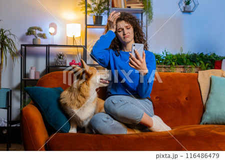 Upset displeased woman using smartphone sitting beside corgi dog loses lottery results or bad news Upset displeased woman using smartphone sitting beside corgi dog loses lottery results or bad news 116486479