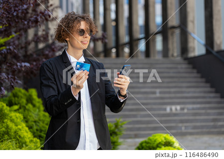 Happy businessman using smartphone and credit card for online shopping standing on city street Happy businessman using smartphone and credit card for online shopping standing on city street 116486490