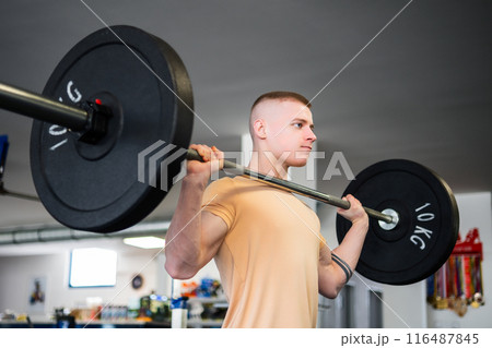Young blond bodybuilder lifts a barbell in a gym 116487845