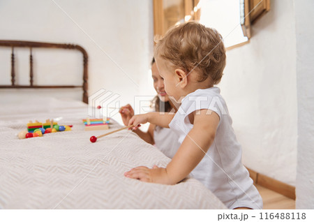 Siblings playing with colorful toys on a bed in a bright, cozy bedroom Siblings playing with colorful toys on a bed in a bright, cozy bedroom 116488118