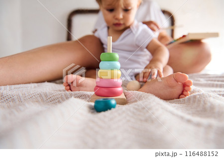 Cute toddler playing with colorful stacking toy at home with parent in background 116488152