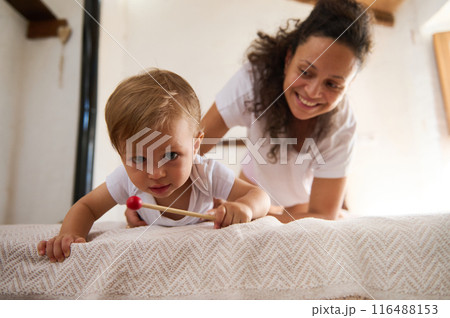 Happy mother playing with her baby boy on the bed in a cozy home interior 116488153