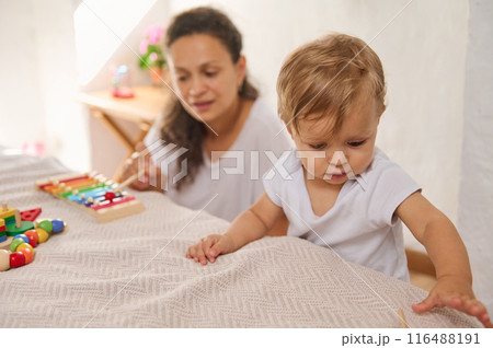Mother and baby bonding time while playing with colorful toys in a warm home environment 116488191