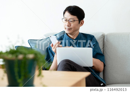 ソファでパソコンとスマホを操作するミドル男性 ソファでパソコンとスマホを操作するミドル男性 116492013