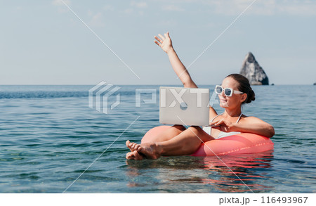 Woman freelancer works on laptop swimming in sea on pink inflatable ring. Happy tourist in sunglasses floating on inflatable donut and working on laptop computer in calm ocean. Remote working anywhere Woman freelancer works on laptop swimming in sea on pink inflatable ring. Happy tourist in sunglasses floating on inflatable donut and working on laptop computer in calm ocean. Remote working anywhere 116493967