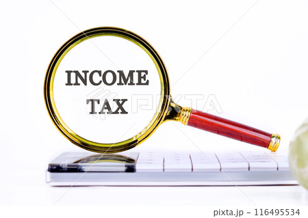 Conceptual income tax symbol. Copy space. Words INCOME TAX through a magnifying glass standing on a calculator on a white background Conceptual income tax symbol. Copy space. Words INCOME TAX through a magnifying glass standing on a calculator on a white background 116495534