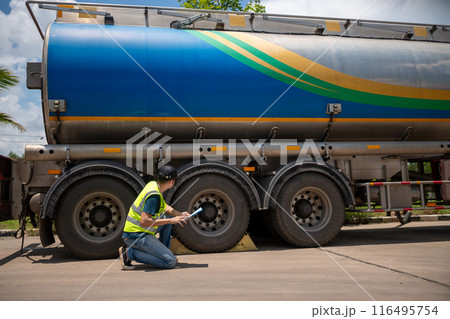 A man is kneeling down next to a large blue and green tanker truck A man is kneeling down next to a large blue and green tanker truck 116495754