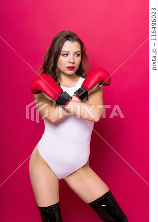 An attractive young brunette woman in boxers gloves, studio shot red background 116496023