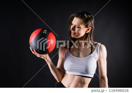 Sportive caucasian cross fit woman with fitness ball, look at camera. Studio dark yellow background 116496026
