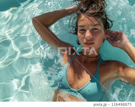 serene woman in a blue bikini is gracefully floating in the crystal-clear water, embodying tranquility and beauty in the natural surroundings. 116498873