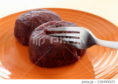 オレンジ色のお皿に盛ったおはぎをフォークで切る 116499325