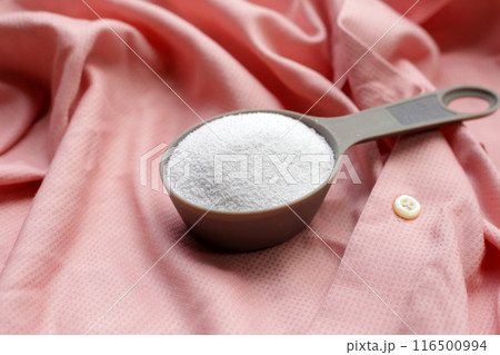Detergent powder in measuring spoon on cloth before washing. Laundry concept. 116500994