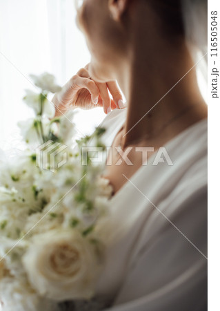 The morning of the bride, a woman wearing a white silk robe holds a wedding bouquet. Close-up photo. The morning of the bride, a woman wearing a white silk robe holds a wedding bouquet. Close-up photo. 116505048