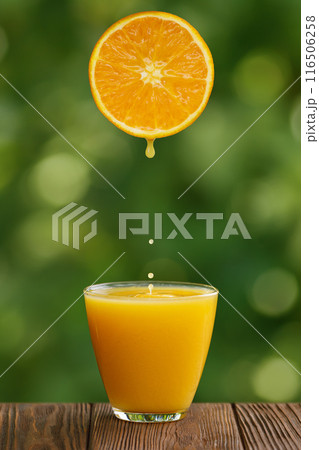 glass of orange juice with splash and falling drops on table with green garden on the background glass of orange juice with splash and falling drops on table with green garden on the background 116506258