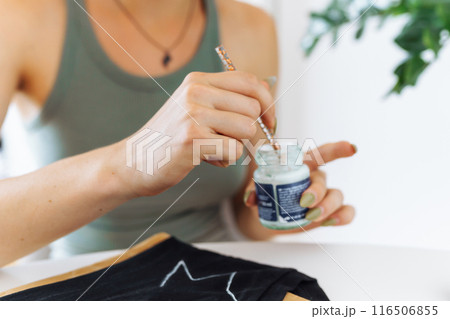 young woman draws picture on clothes with paints, handmade craft work. Customization 116506855