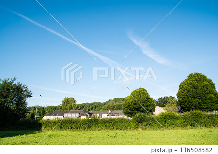 真っ青な青空に残った飛行機雲の下の明るい日差しが当たるフィールドと歴史的な住宅　南ウェールズにて 116508382